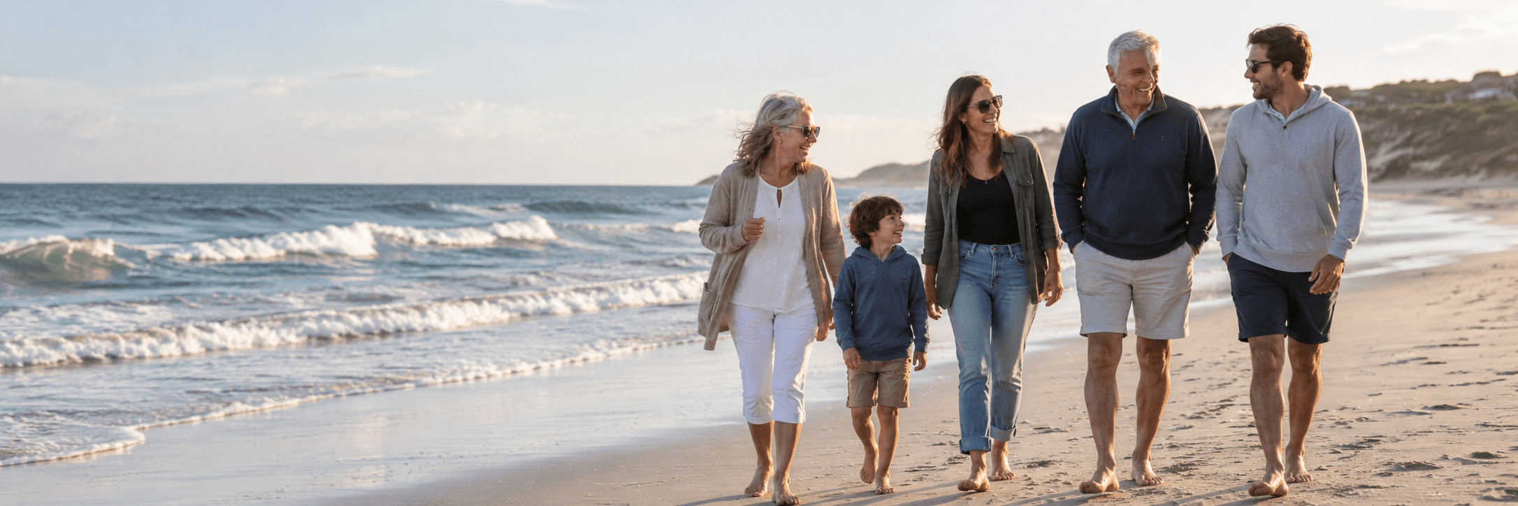 A family of four walking along the beach during sunset.